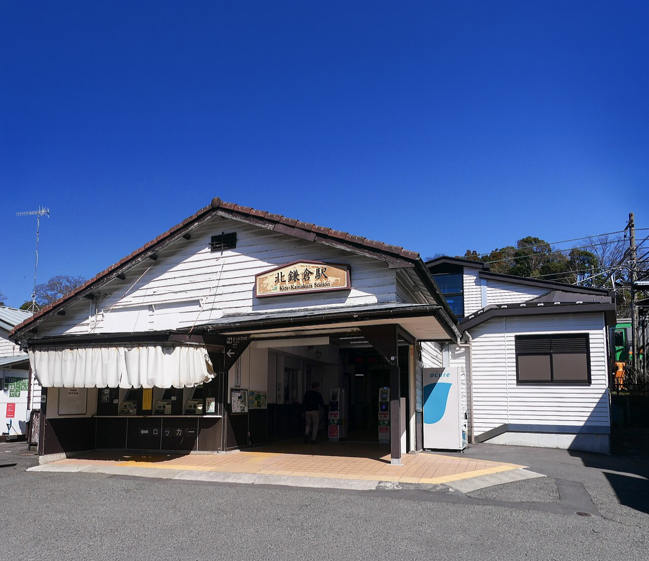 The white wooden station building of Kita-Kamakura Station, its name board under the gable, beneath a clear blue sky
